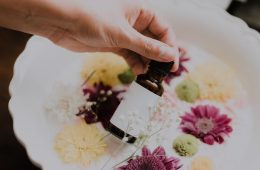 a woman holding a bottle of essential oils with a milk bath and flowers in the background