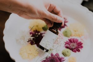 a woman holding a bottle of essential oils with a milk bath and flowers in the background