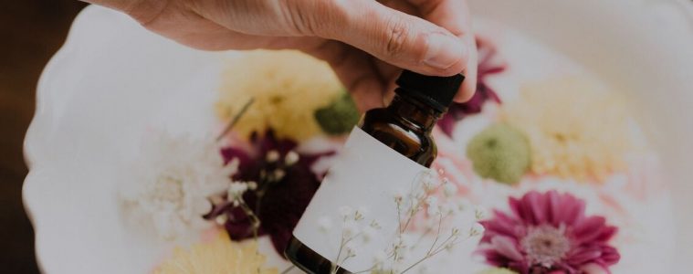 a woman holding a bottle of essential oils with a milk bath and flowers in the background