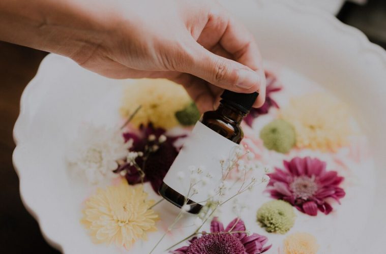 a woman holding a bottle of essential oils with a milk bath and flowers in the background