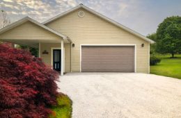 Freshly sealed gravel driveway leading to garage house.