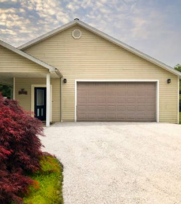 Freshly sealed gravel driveway leading to garage house.