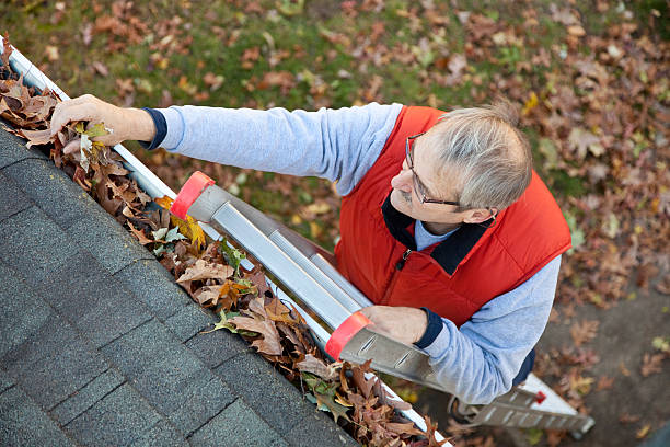 Senior man cleaning leafs out of gutter, for winter.