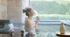 Lady relaxing sitting in hot bath tub with towel on head