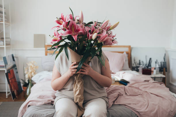 Woman sitting on her bed and holding a bouquet of pink lillies