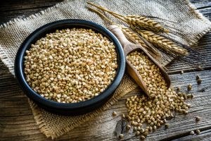 Wholegrain buckwheats in a black bowl on rustic wooden table.