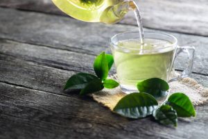 Glass cup of green tea with fresh tea leaves on wooden table.