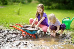 Two little girls playing in a large wet mud puddle on sunny summer day.