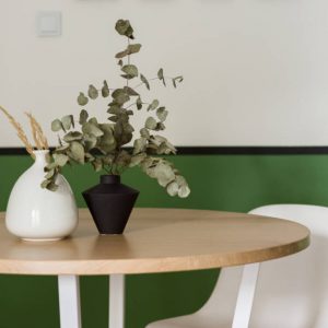 Close-up on round and wooden dining table with stylish vases and plants paired with olive green colour