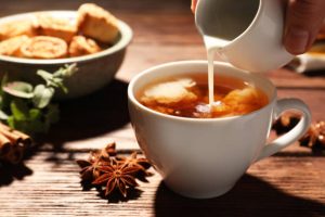 Woman pouring milk into cup of tea at wooden table