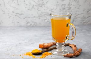 Turmeric tea in the glass with turmeric sticks and powder on the surface.