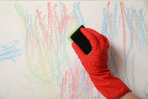 Woman erasing child's drawing from white wall, closeup