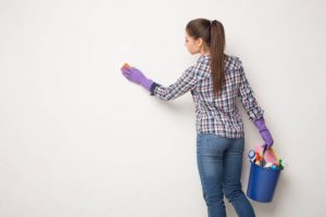 Woman wiping white with dry cloth, cleaning crayon marks on walls