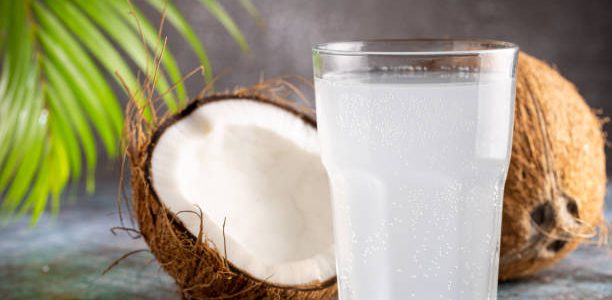 Glass with fresh coconut water and coconuts on the table.