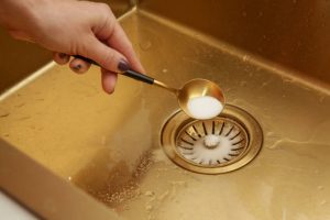 Cleaning kitchen sink with bakIng soda to keep sinks draining system clog free