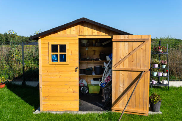 A wooden garden shed standing on a concrete foundation in a garden, flowers and tools visible.