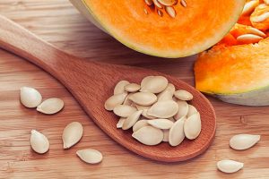 Pumpkin seeds inside of wooden spoon near cut pumpkins
