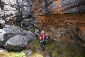 Rear view of a couple hiking through a crack in the rocky mountains, they are hiking through the Cederberg Mountains near Cape Town. Man exploring the beautiful outdoors.