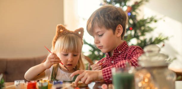 Children paint wooden toys near Christmas tree at home